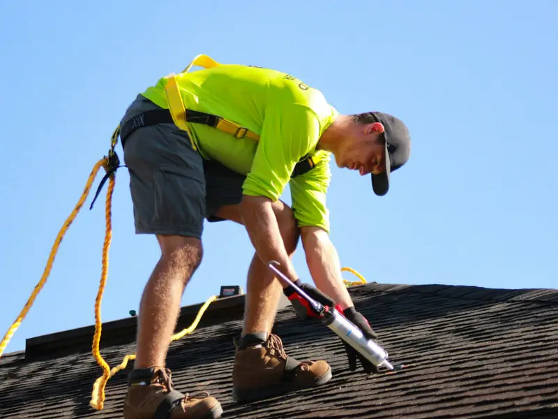 Roofer sealing flashing on a dark shingle roof